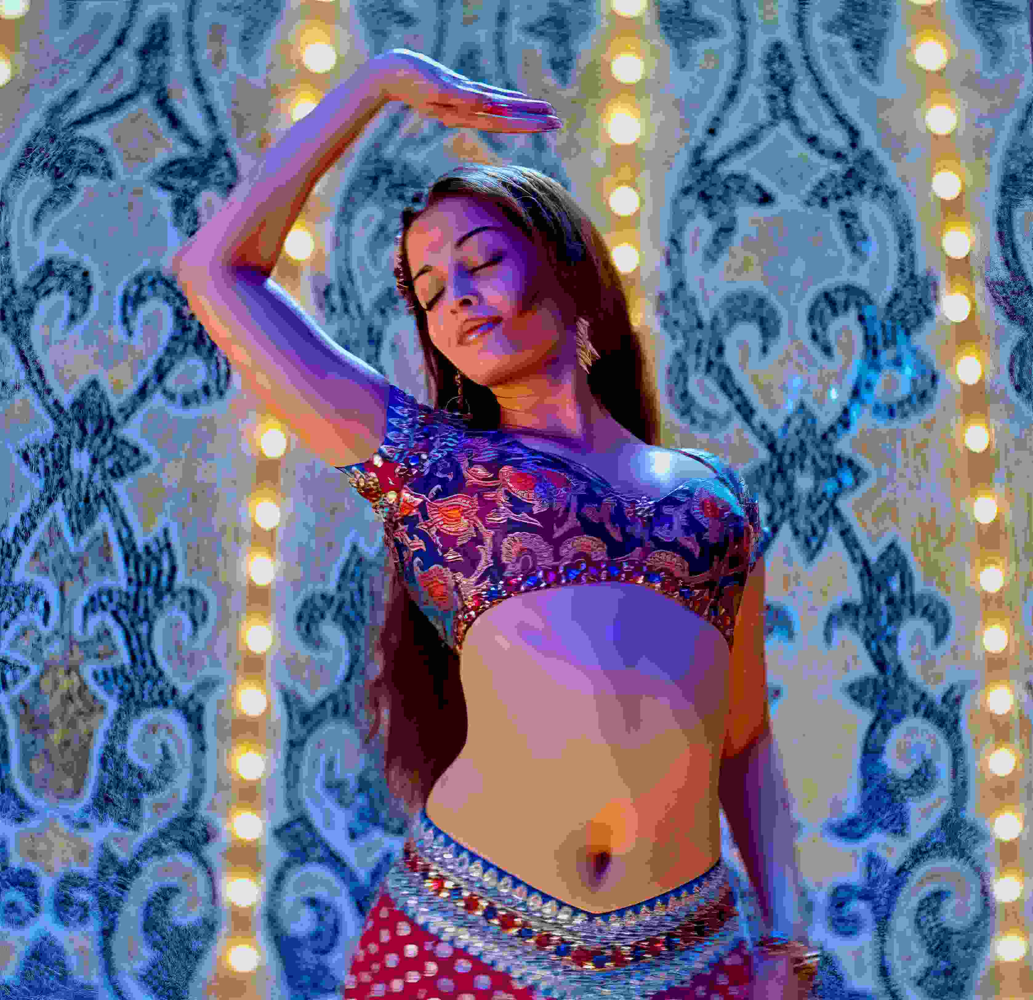 Danseuse bras levé en costume bleu et violet, devant un fond à motifs