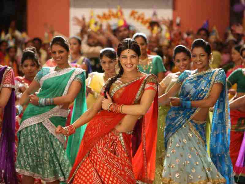 Un grand groupe de danseuses en saris colorés, sur une scène de film