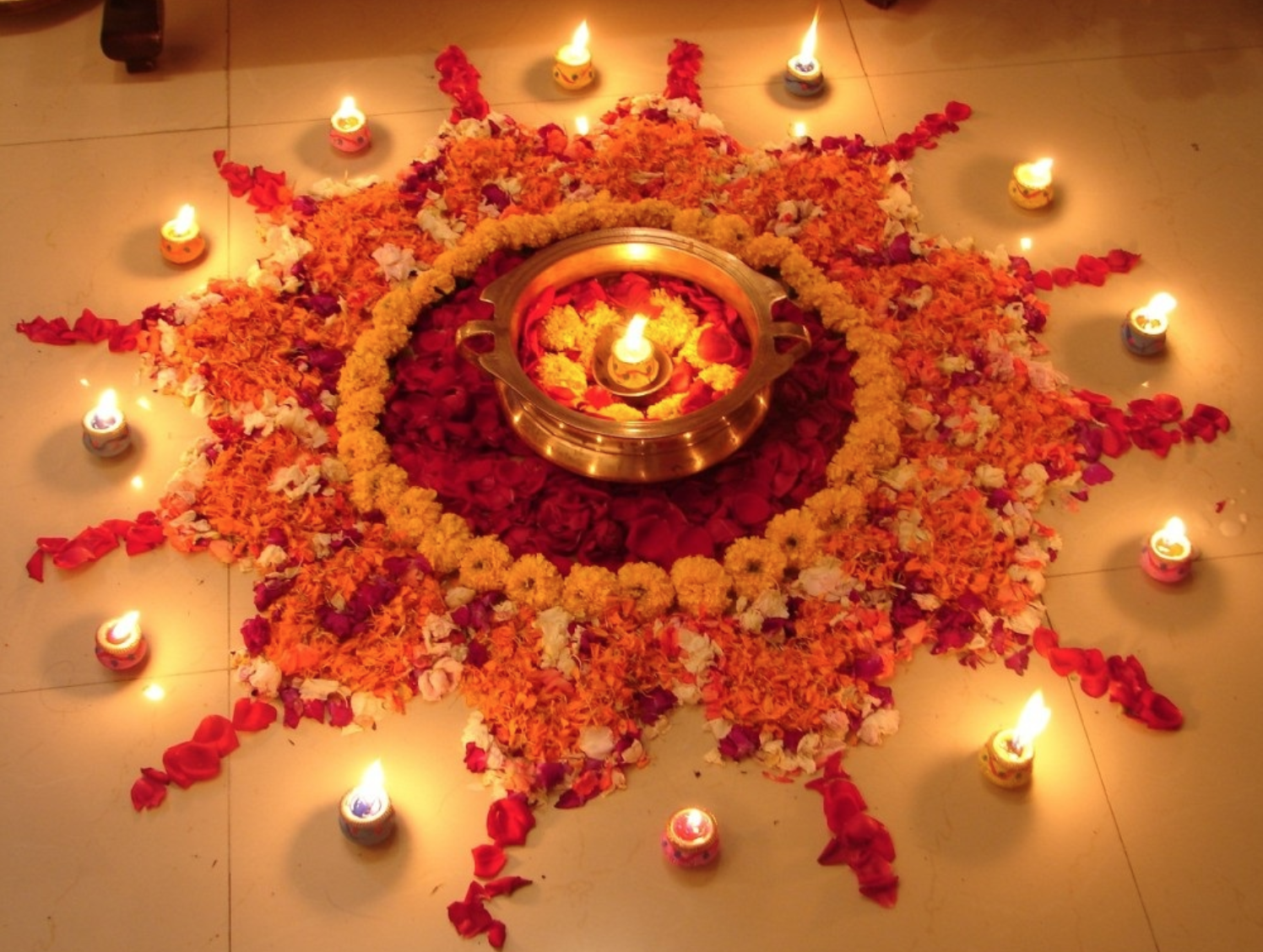 Rangoli de fleurs orange et rouges en cercle, parsemé de bougies allumées