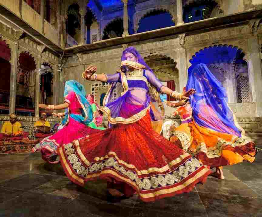 Trois danseuses aux jupes tournoyantes multicolores, devant un palais