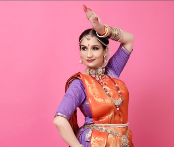 Danseuse de Kathak en posture classique, bras au-dessus de la tête, sur fond rose