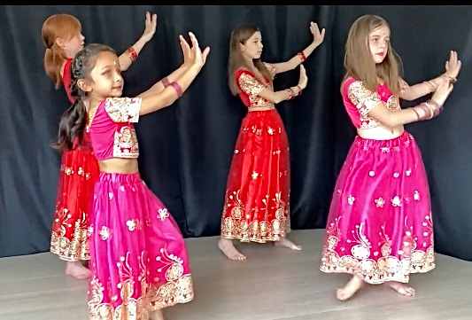 Quatre fillettes en costumes de danse indienne rouge et rose, bras levés