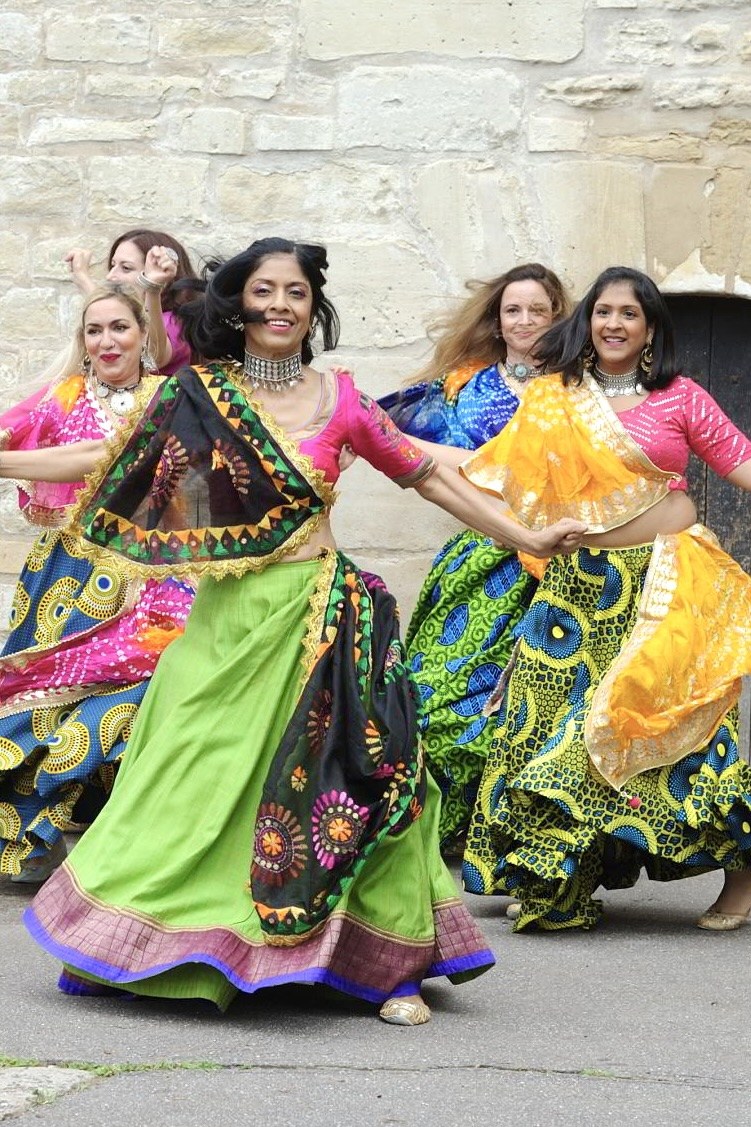 Quatre danseuses en jupes colorées de garba, devant un mur de pierre