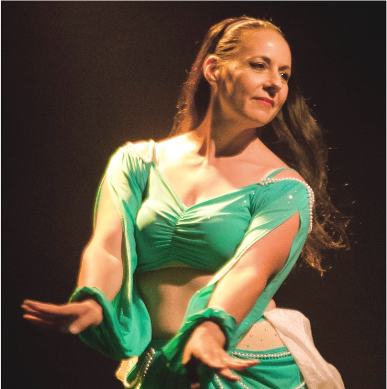 Sareea en costume de danse orientale blanc, mains sur les hanches, devant un fond vert au motif de mandala
