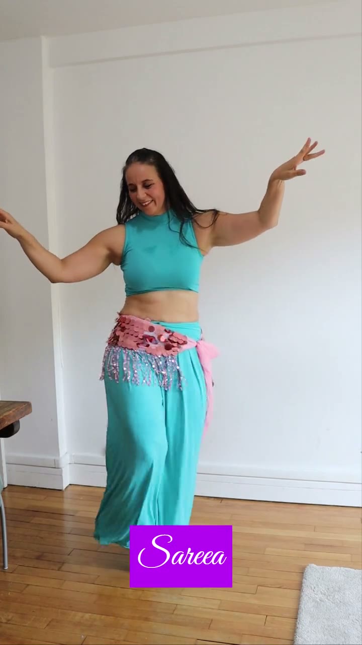 Sareea en haut et pantalon turquoise, ceinture à franges rose, bras levés dans une pièce claire